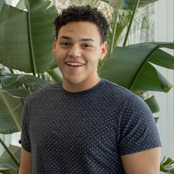 Young man standing in front of a plant smiling.